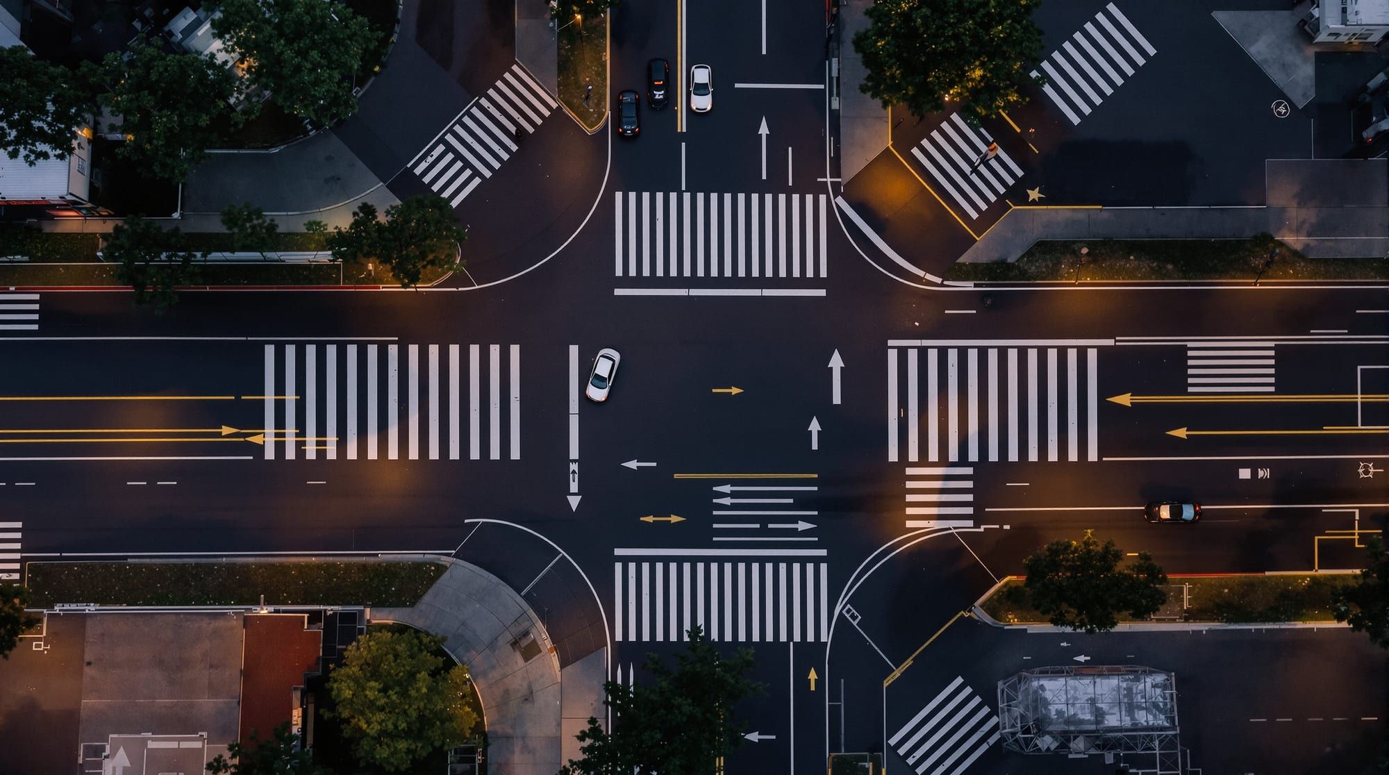Drone view straight down on a city intersection at dusk, crosswalks and lane arrows