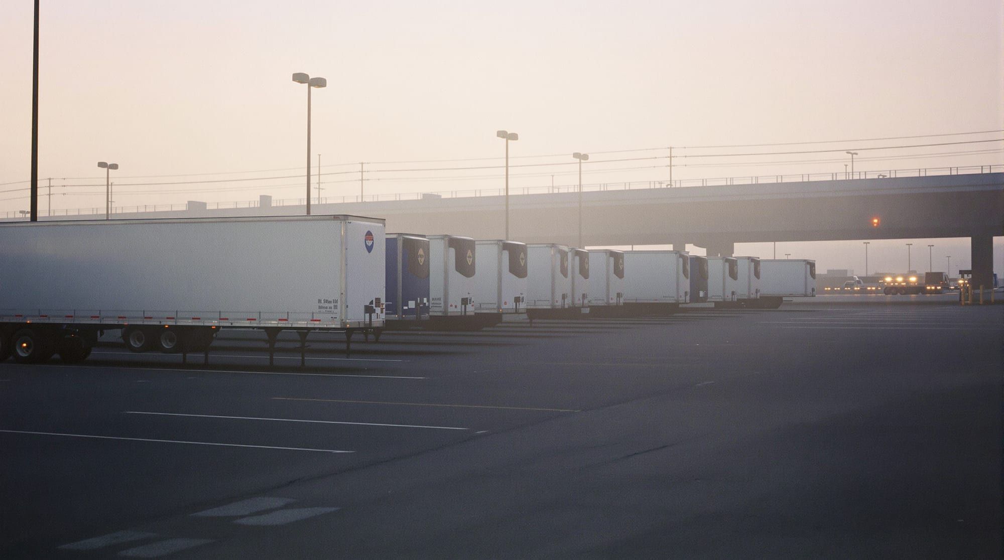 Row of parked trailers at a truck stop lot at dawn in light mist